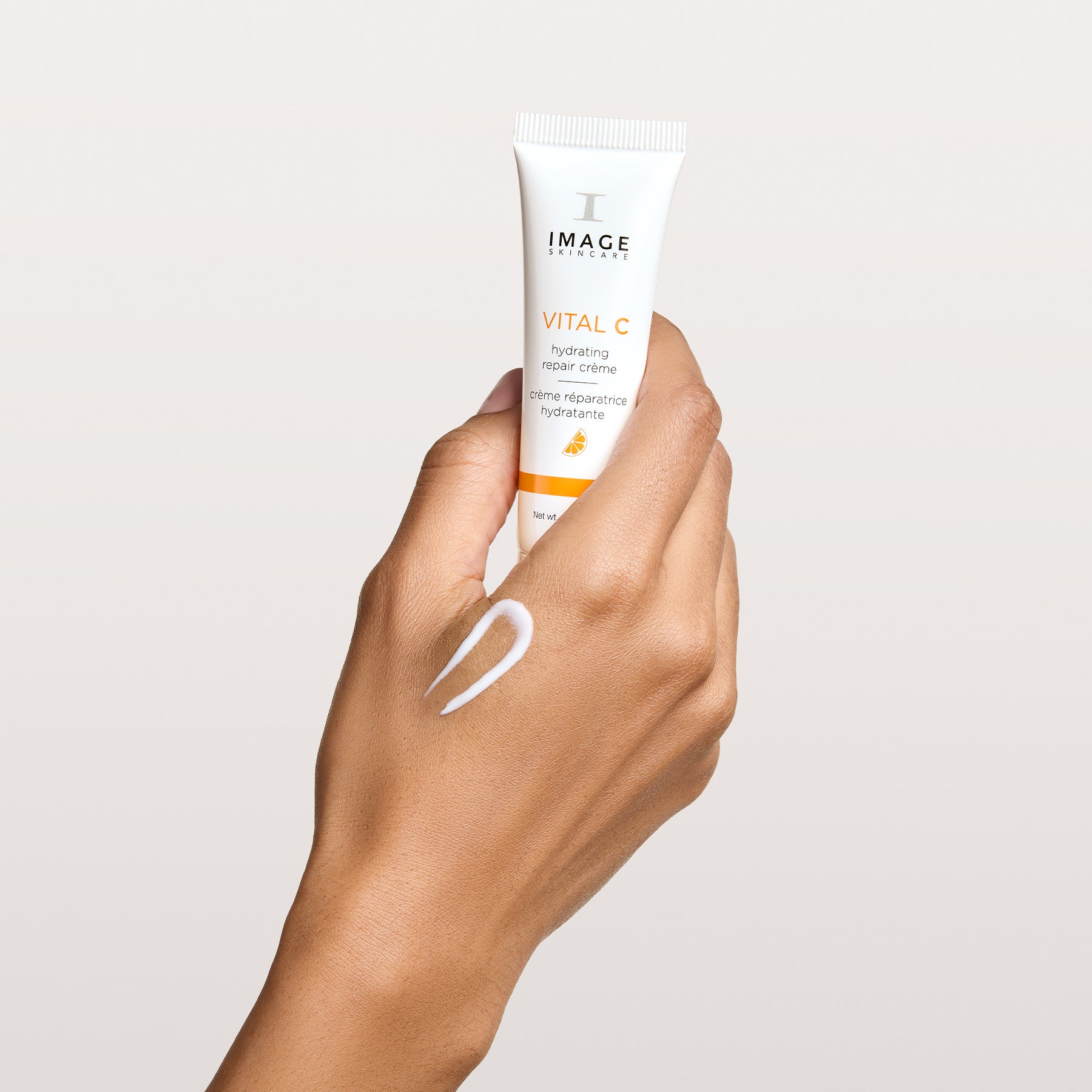 model hand holding travel size repair creme with texture swatch on hand